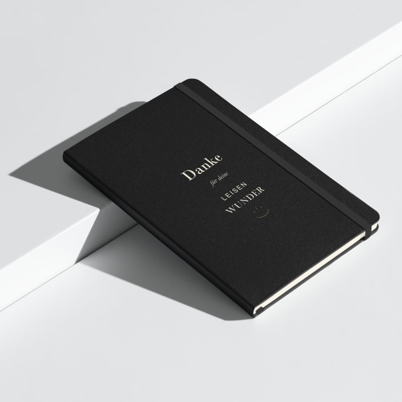 Schwarzes Hardcover-Notizbuch „Danke für deine leisen Wunder“, schräge Ansicht mit heller Typografie.