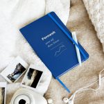 Blaues Hardcover-Notizbuch „Fernweh passt auf diese Seiten“ mit cremefarbener Typografie, schräge Ansicht auf hellem Stoff