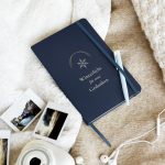 Notizbuch in Navy „Winterlicht für neue Gedanken“ mit Schneekristall, schräg auf hellem Stoff fotografiert