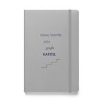 Silbernes Hardcover-Notizbuch „Kleine Schritte füllen große Kapitel“ mit violetter Typografie und Treppenmotiv