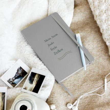 Silbernes Hardcover-Notizbuch mit dunkelgrüner Schrift und Linienmotiv, schräg auf hellem Stoff fotografiert