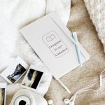 Weißes Lese-Notizbuch mit Buchmotiv und weinroter Schrift, schräg auf hellem Stoff fotografiert