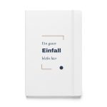 Weißes Hardcover-Notizbuch „Ein guter Einfall bleibt hier“ mit dunkelblauer Schrift und kupferbraunen Winkeln – Vorderansicht